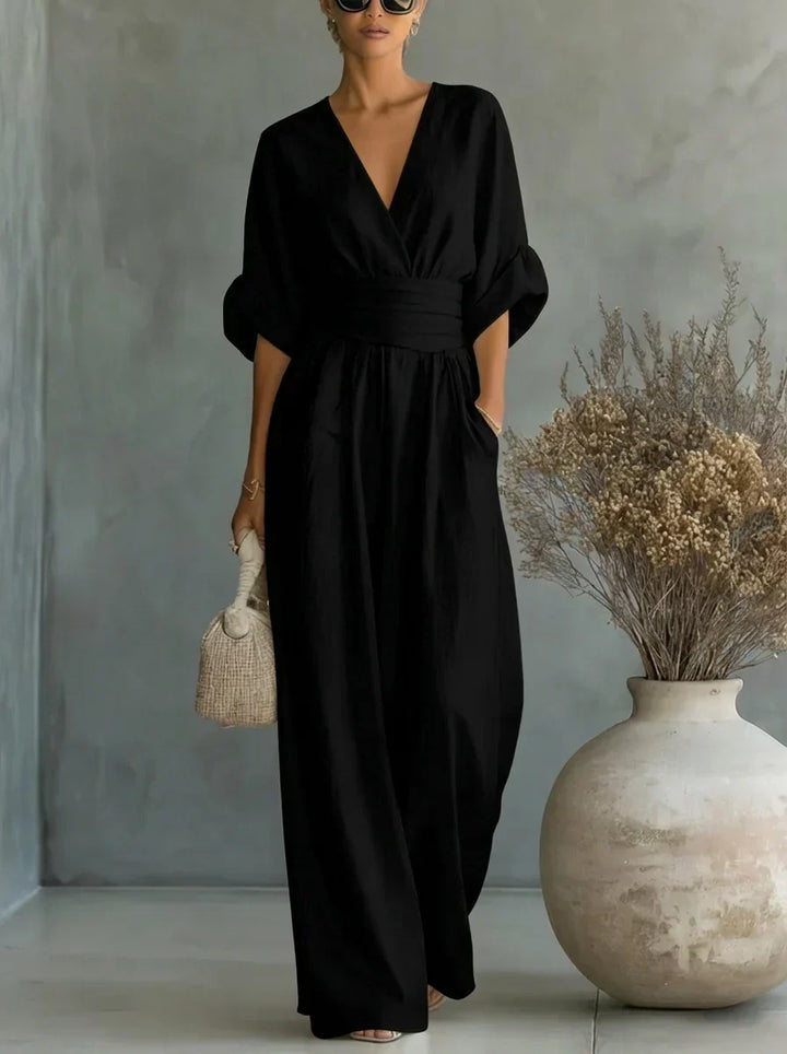 Vestido largo negro con escote en V y cintura fruncida, mangas caídas y falda amplia.